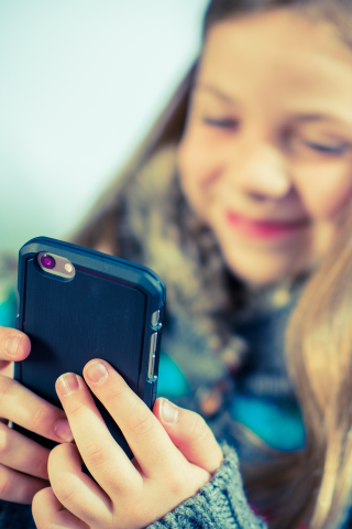 Pige smiler, mens hun kigger på telefon